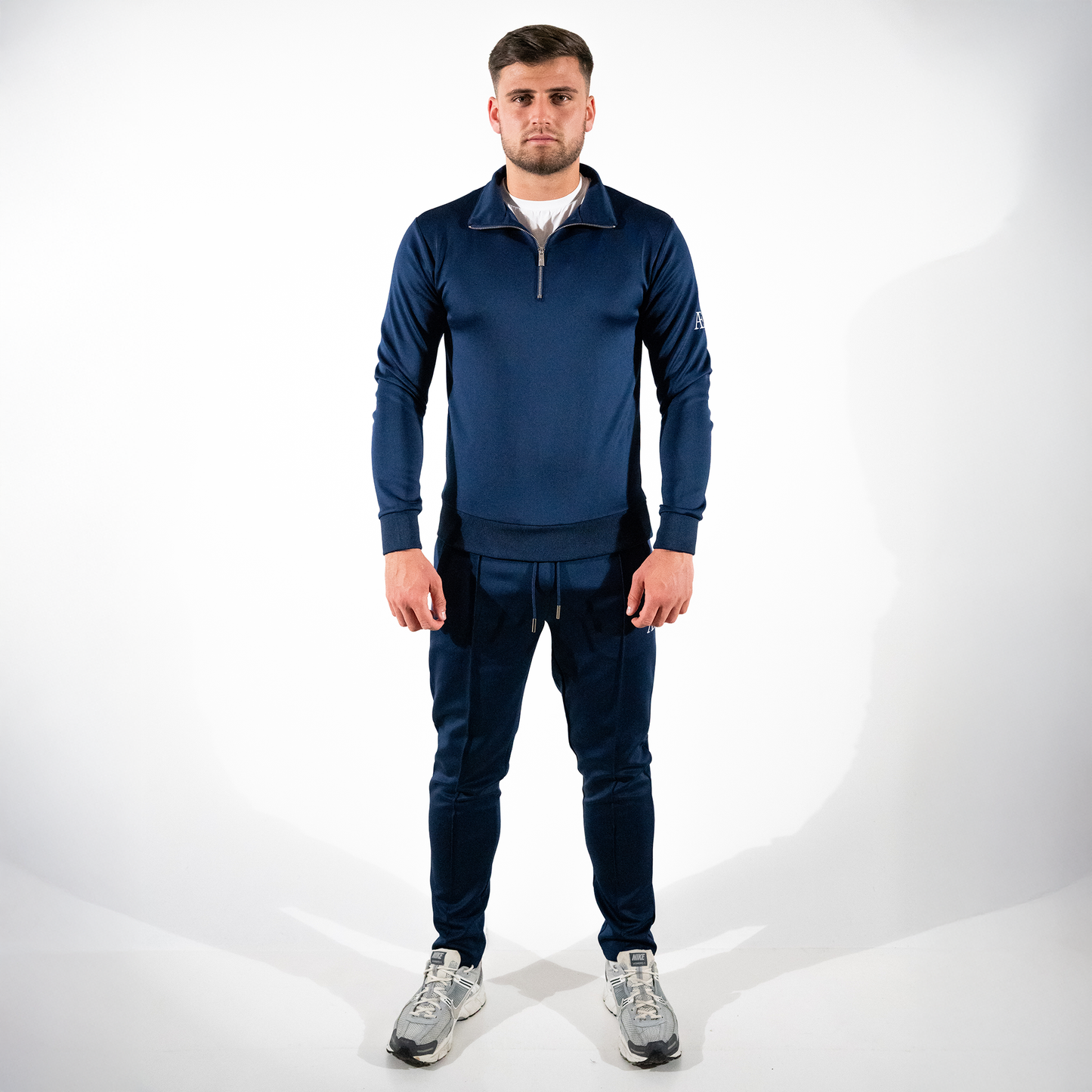 Man modeling navy slim-fit bottoms with matching quarter-zip against white backdrop