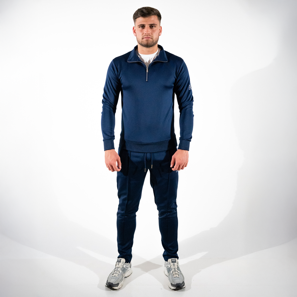 Man modeling navy slim-fit bottoms with matching quarter-zip against white backdrop