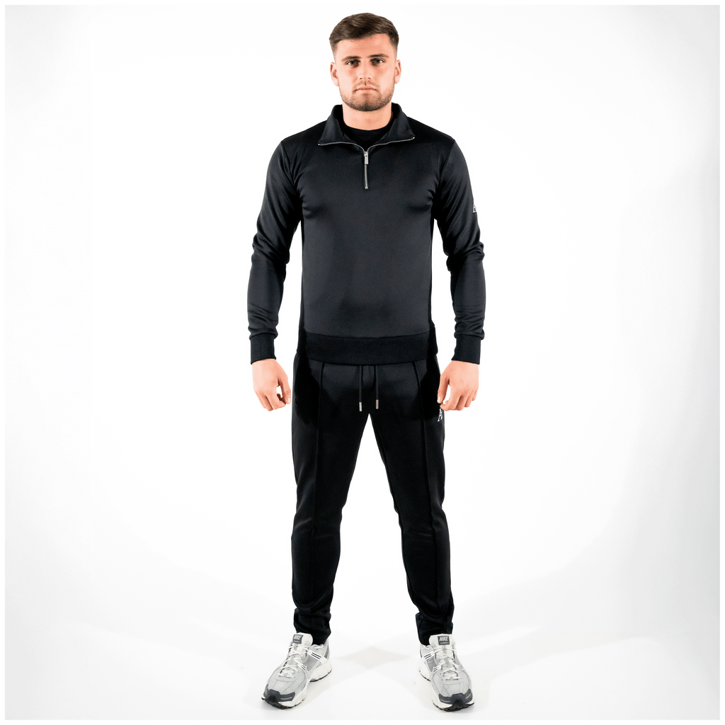Model in black slim-fit bottoms and matching quarter-zip, minimal AÉCLO branding