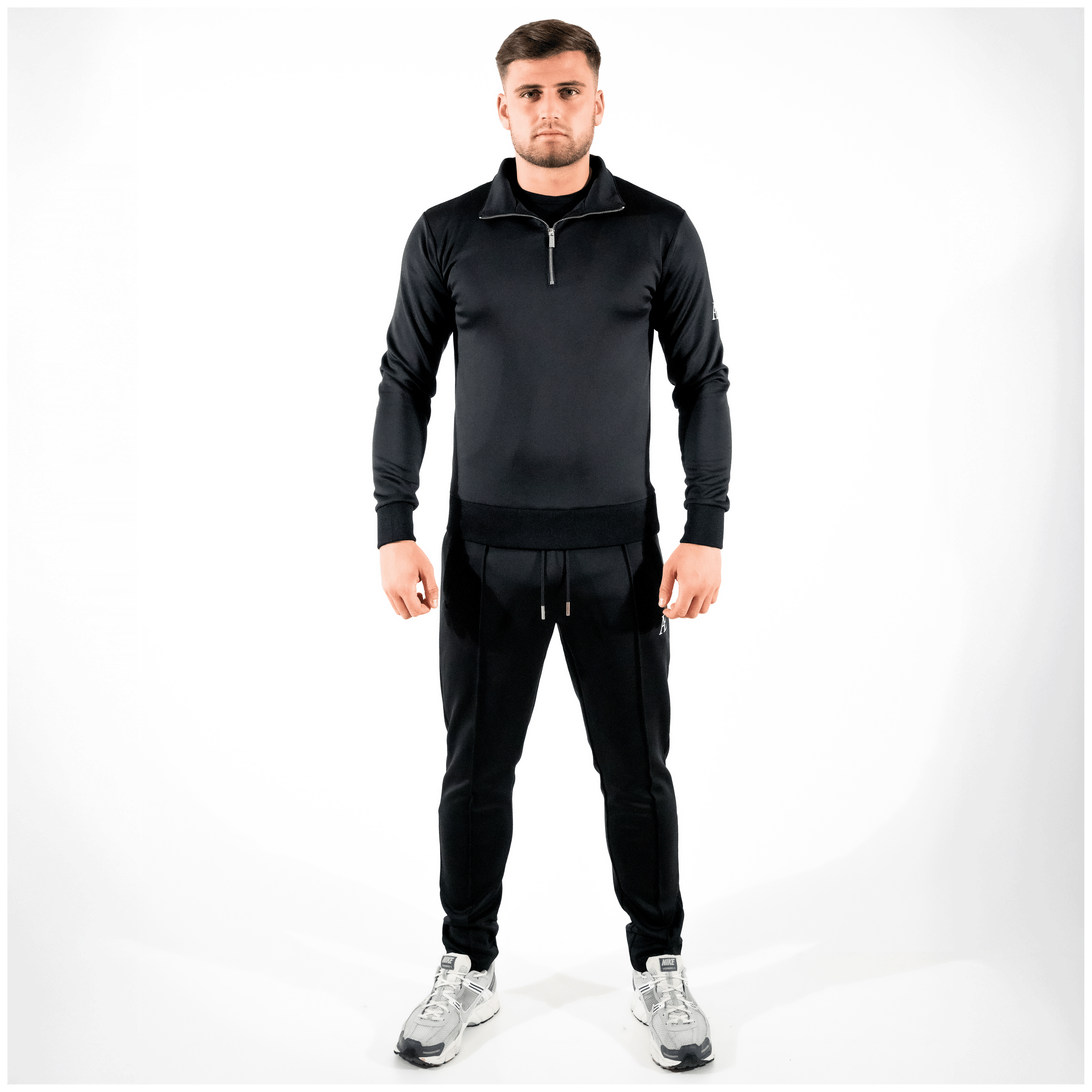 Model in black slim-fit bottoms and matching quarter-zip, minimal AÉCLO branding