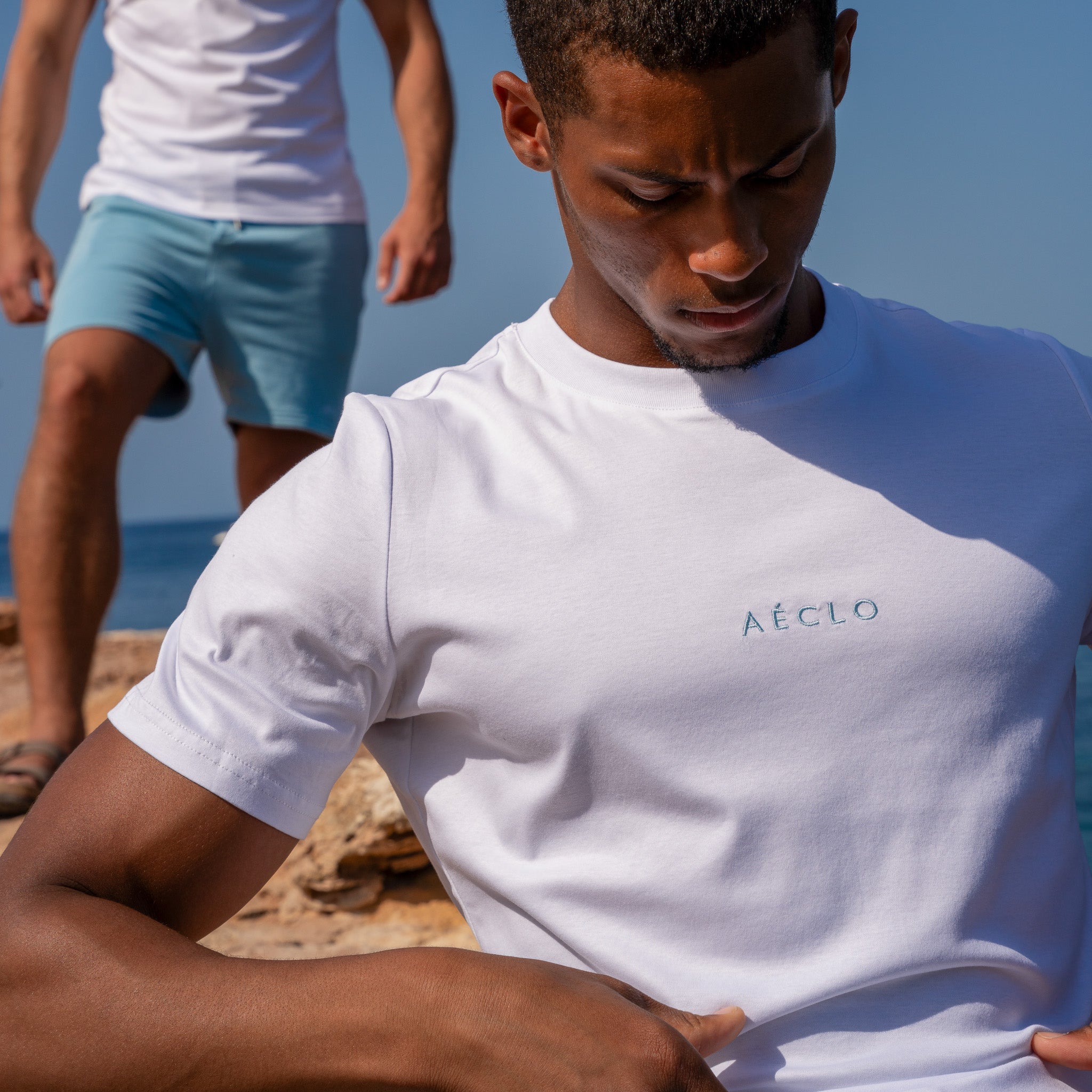 Man wearing a white t-shirt with 'Aéclo' logo on a beach