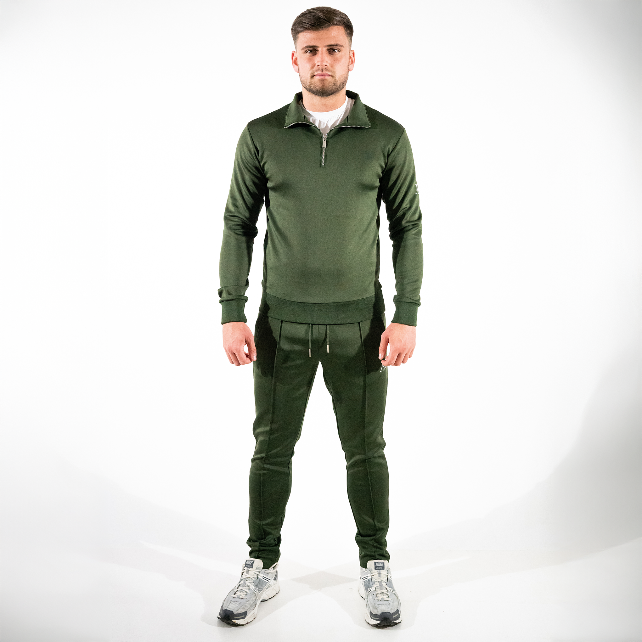 Model wearing forest green quarter-zip and matching slim-fit bottoms on white backdrop